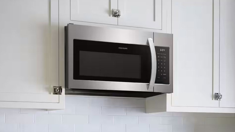 A stainless steel Frigidaire Over-the-Range Microwave is surrounded by white kitchen cabinets