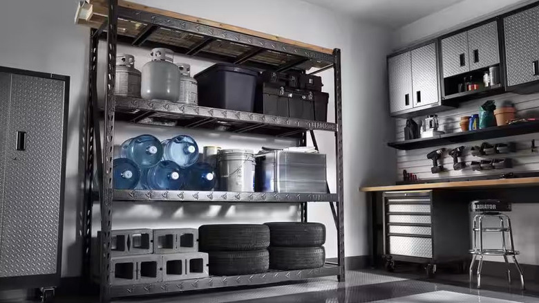 Tires, water jugs, propane tanks, and storage boxes sit on a black metal shelf in a garage workshop