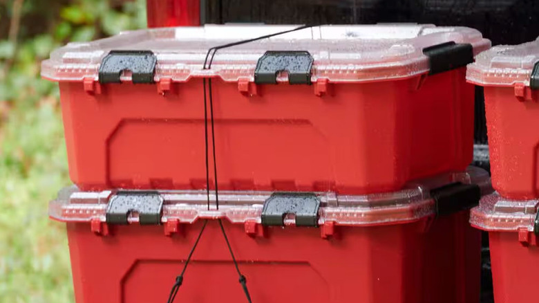 Two red stackable storage containers tied together sit on the bed of a black truck