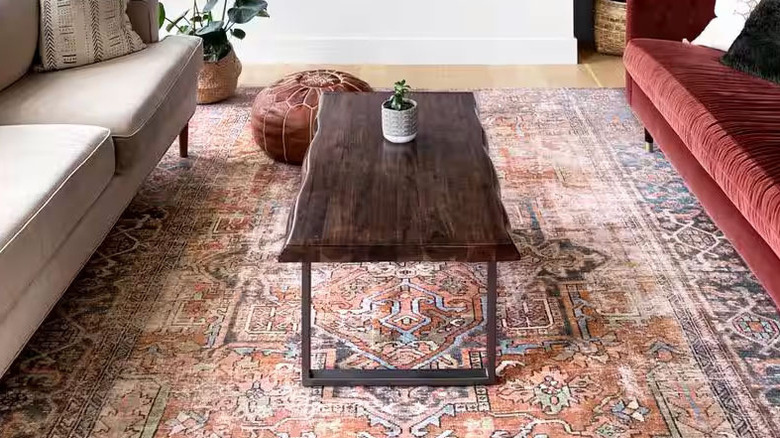 A wooden coffee table sits on top of a colorful living room rug