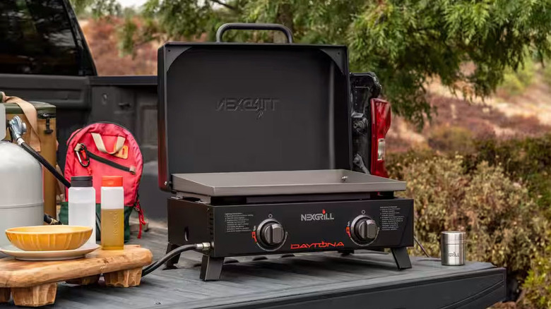 A small portable grill sits on the bed of a black truck