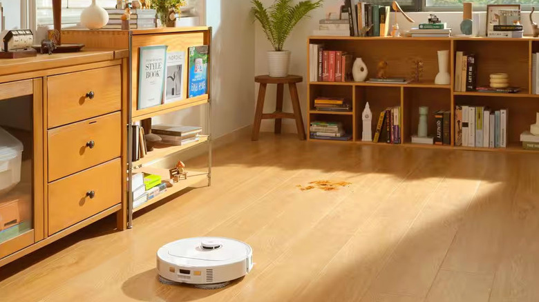 A small white robotic vacuum cleans a wooden living room floor