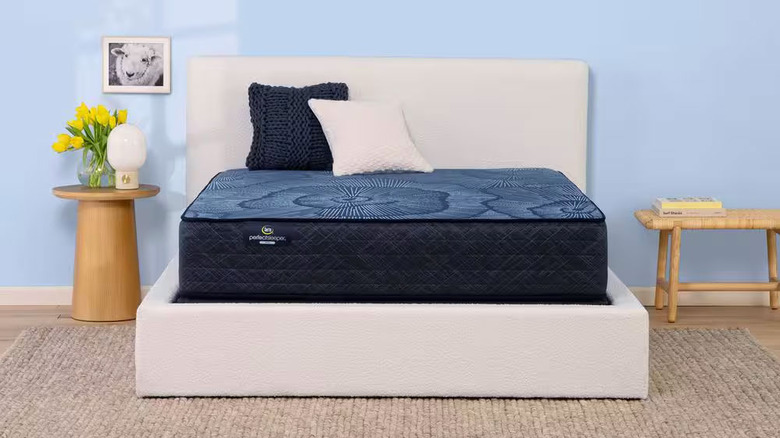 A dark blue Serta mattress sits on a white bedframe