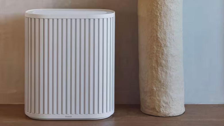 A white air purifier sits next to a decorative pillar on a hardwood floor