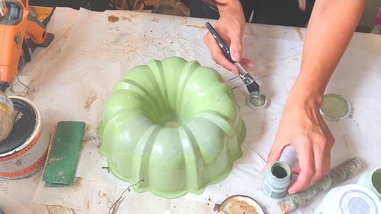 Woman painting Bundt pan light green for decor on art tarp with crafting materials