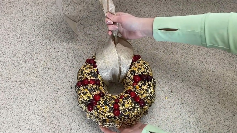 Woman holding Bundt cake-shaped bird feed wreath with stylish ribbon over stone-like surface