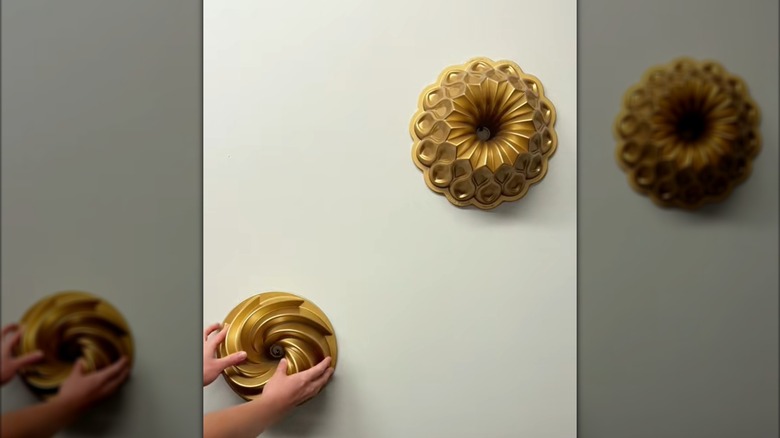 Glossy gold Bundt pans tacked on basic white wall for decor