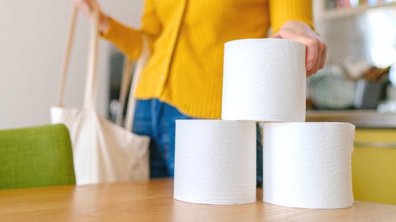 Person putting rolls of toilet paper on a wood table