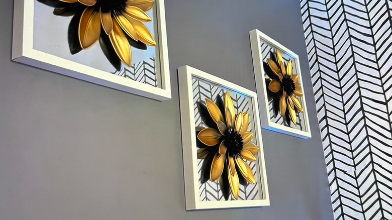 Three 3D Floral framed art pieces hang on a gray wall next to a chevron striped accent wall