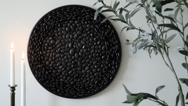 A black stone covered wall decoration is flanked by tapered candles and a leafy plant