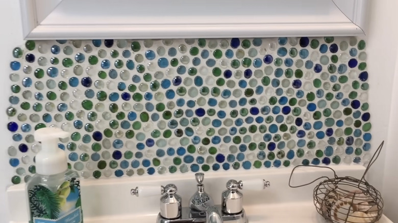 The wall behind a bathroom sink is covered in blue and green gemstones