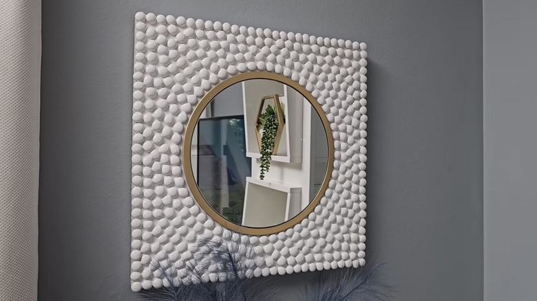 A circular mirror surrounded by painted white gemstones hangs on a gray wall