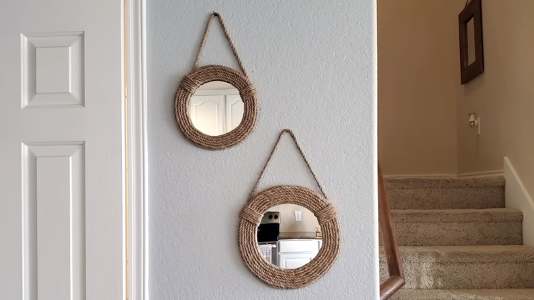 Two nautical rope framed mirrors hang on the wall between a white door and staircase
