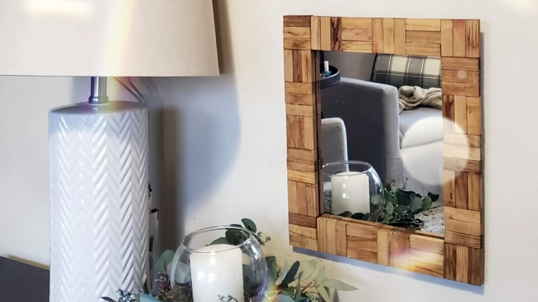 A Jenga-piece framed mirror hangs on a wall next to a white table lamp