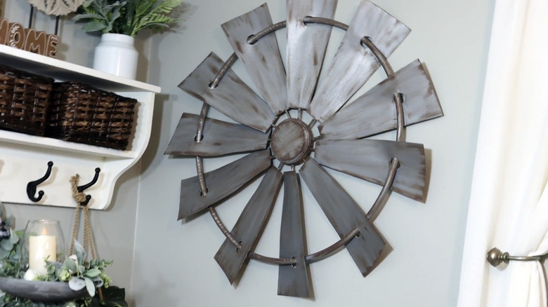 A large farmhouse windmill hangs on a wall next to a decorated shelf