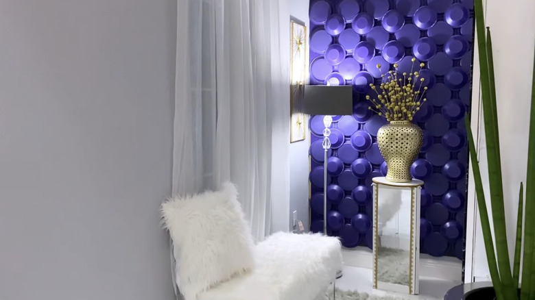 A large gold vase sits on a mirrored table in front of a bold accent wall made with purple paper plates