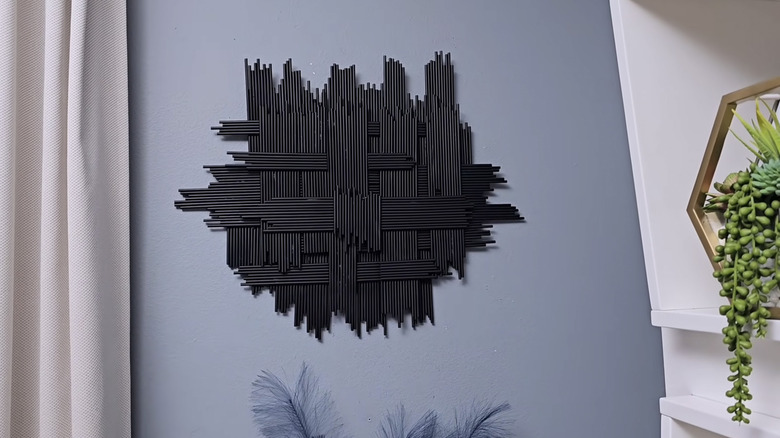 A modern piece of wall art made of spray-painted straws hangs on a light blue wall