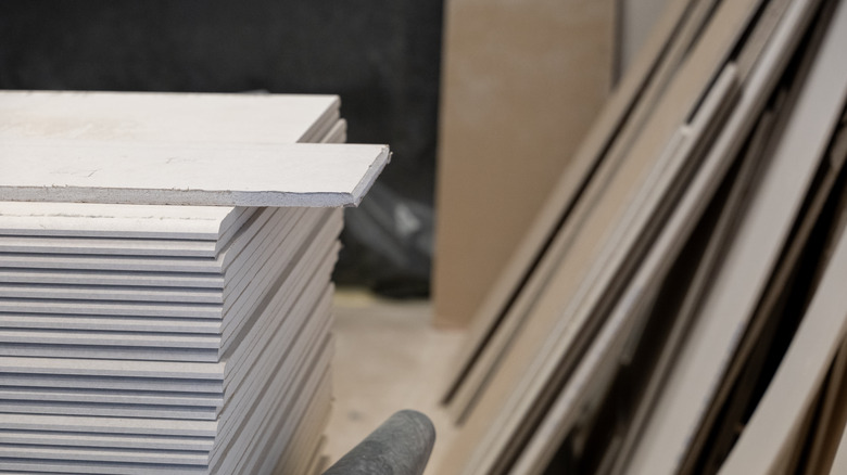 Sheets of drywall are stacked and leaning against a garage wall