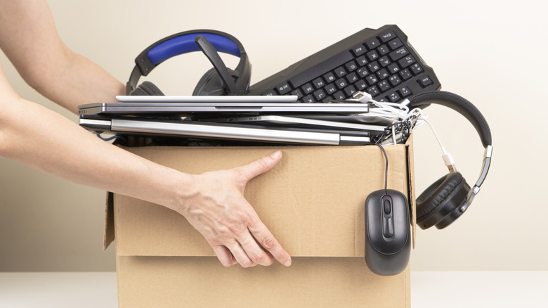 A woman's hands hold a cardboard box full of electronics