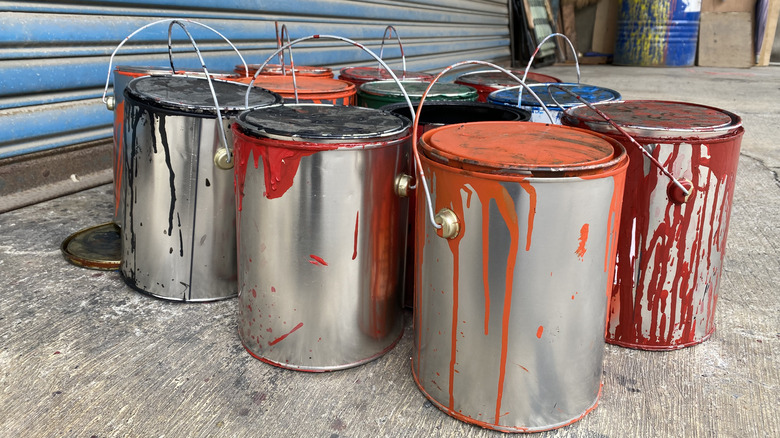 Messy cans of paint sit on a concrete garage floor