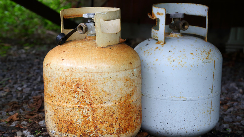Two old propane tanks sit next to each other on the ground