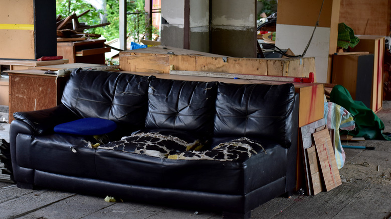 An old black upholstered sofa looks worse for wear in a large garage