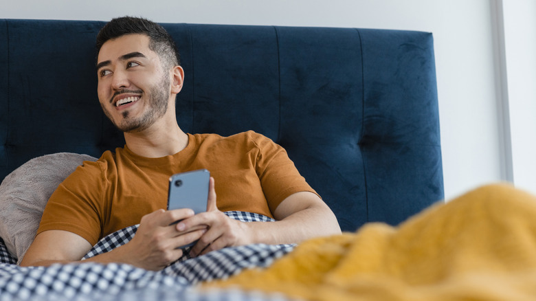 A man lies in his bed, smiling and thinking in a colorful bedroom