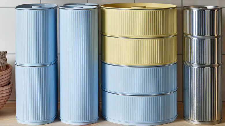Blue, yellow, and stainless steel BETTHAJ Tins from IKEA are stacked next to each other on a wooden kitchen counter