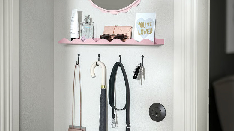 A lighit pink DAGGKAPRIFOL Picture ledge from IKEA containing bottles, glasses, and a card reading 'You Are Loved' hangs on a wall above four hooks containing various items