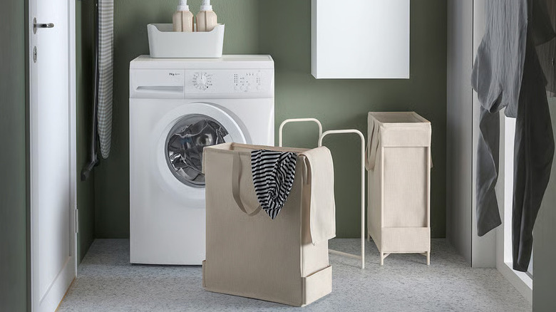 A beige PURRPINGLA Laundry bag with stand from IKEA sits in front of a white washing machine