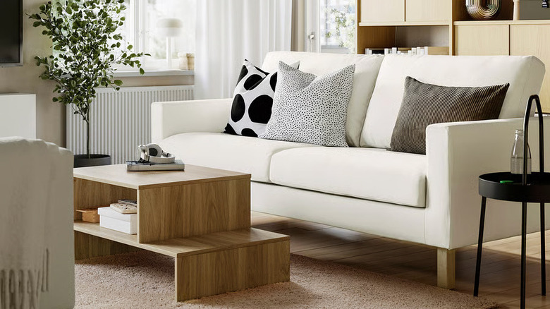 A white SALTSJÖBADEN 3-seat sofa from IKEA sits in a living room next to a wooden coffee table and black side table