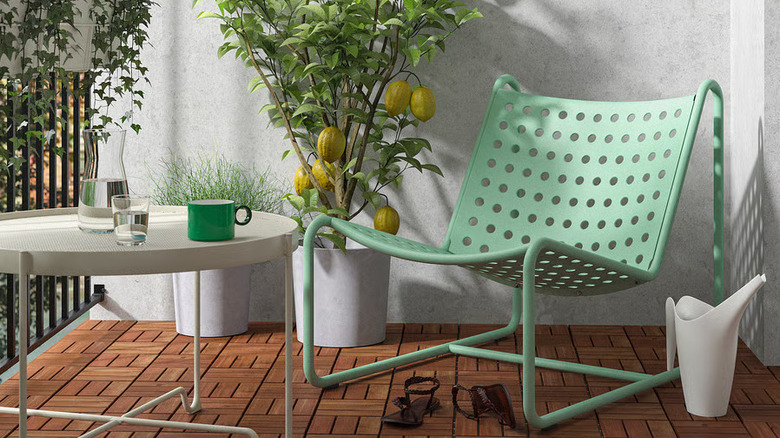 A sea foam green SKOGSÖN Chair sits next to a potted plant and low table on a sunny balcony