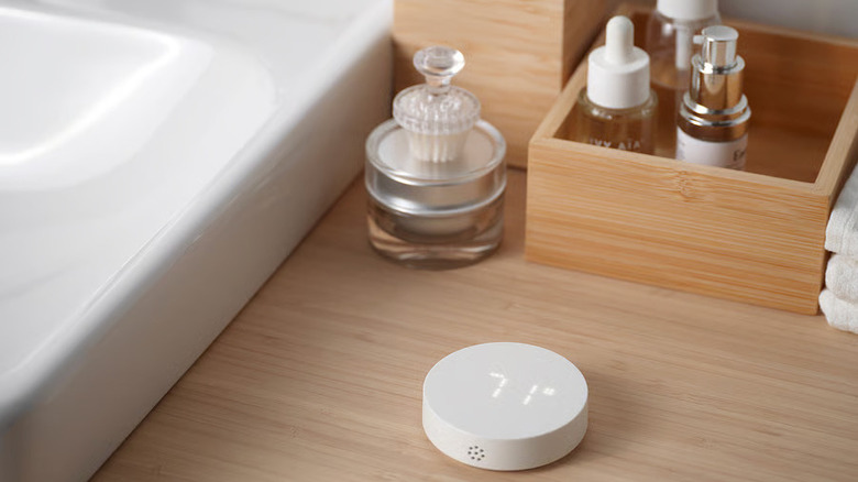 A TIMMERFLOTTE Temperature/humidity sensor from IKEA sits on a wooden countertop near several skincare products