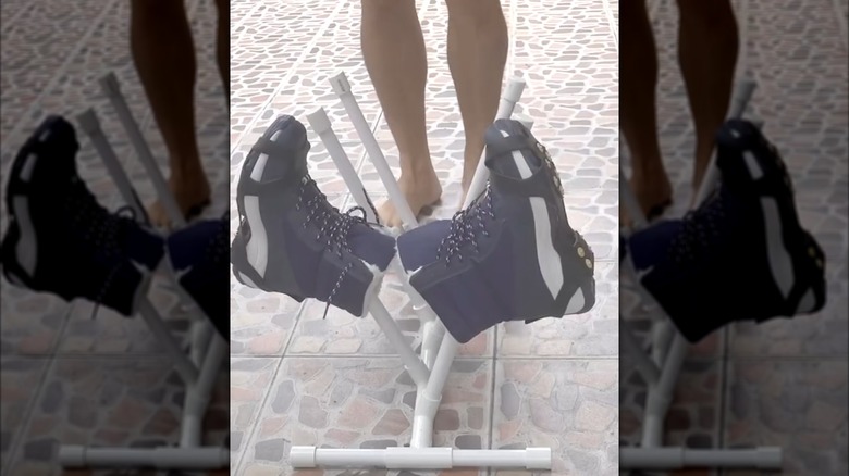 Person standing in front of boots propped up on PVC pipe rack on outdoor mosaic-style tile