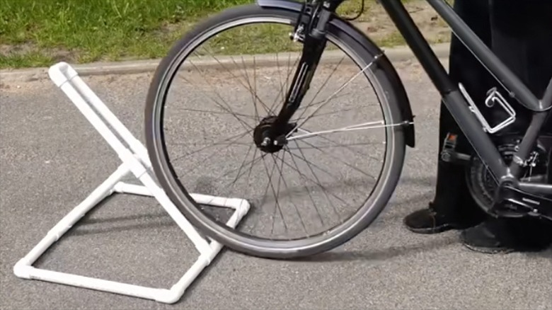Black bike wheel rolling up on PVC pipe rack on asphalt street