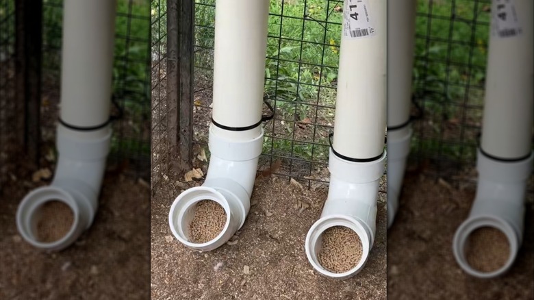 Pair of white chicken tube feeders filled with feed attached to black wire fence