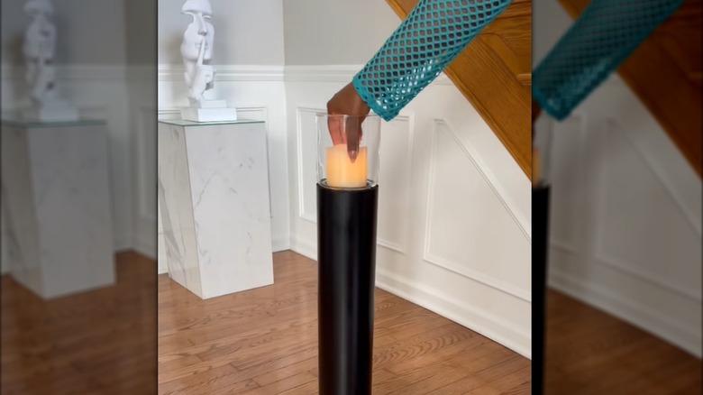 Woman placing electronic candle in black PVC pipe holder in glamorous home