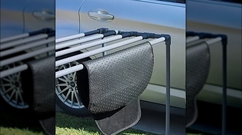 Rubber car mat drying on outdoor pipe stand beside car