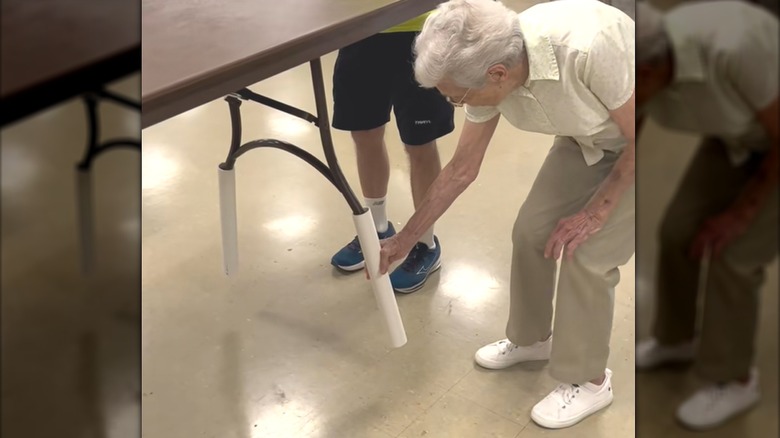 Elderly woman sliding PVC pipe onto foldable table leg for event