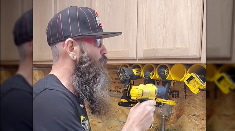 Bearded man storing power tools in hanging PVC pipe organizers in garage