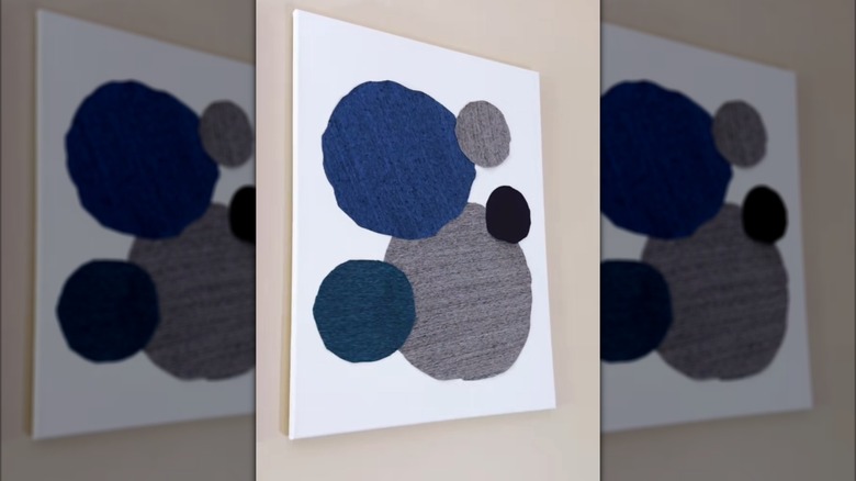 Gray, blue, and black fabric clothing panels cut out onto canvas as abstract wall art on beige wall