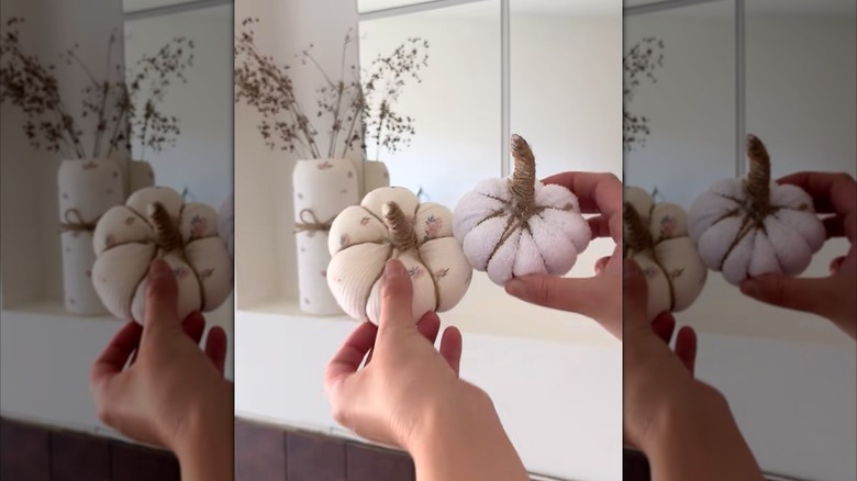 Woman holding up two handcrafted pumpkins from old clothes in front of matching vase display