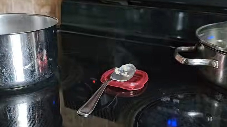 Small red plastic lid used as a spoon rest on a stovetop