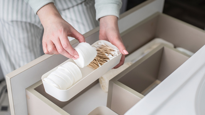 A person organizes cotton rounds and swabs in a bathroom.