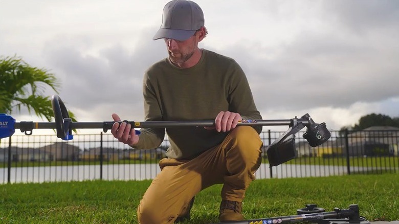 Man assembling a Kobalt string trimmer while crouched on a lawn