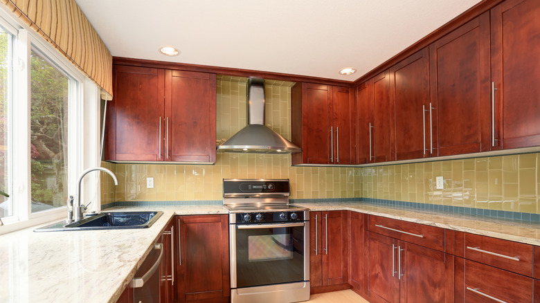 dark wood stained cabinets in outdated kitchen with tile backsplash and window