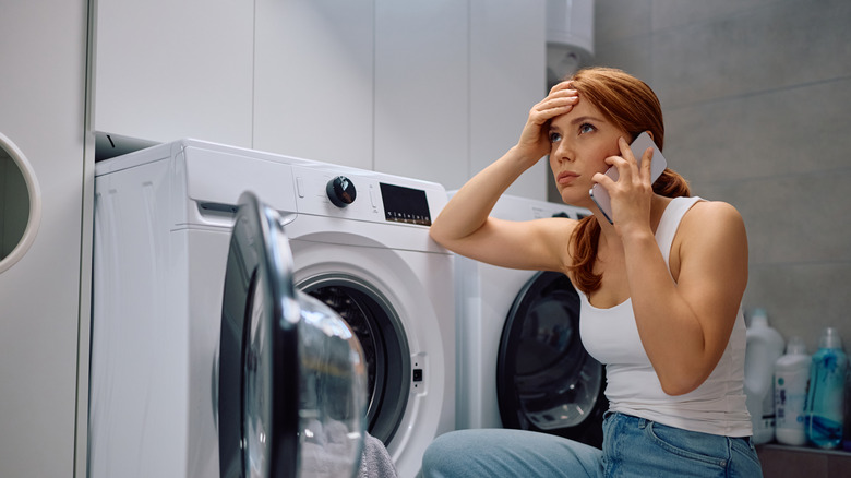 A woman makes a phone call while sitting next to a washing machine