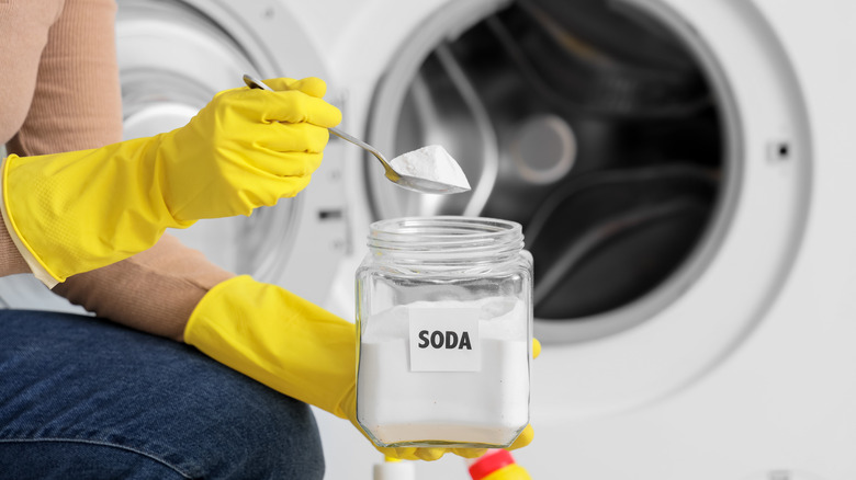 A person wearing gloves scooping baking soda to put in a washing machine