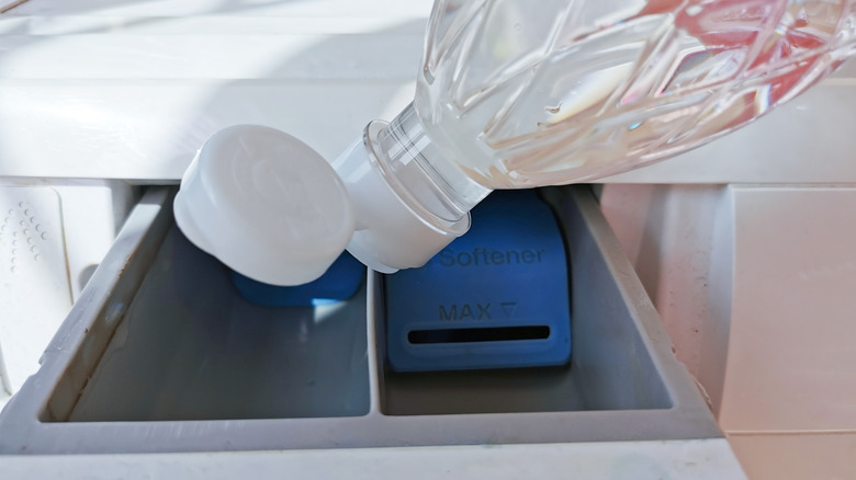 A person pouring white vinegar into a washing machine