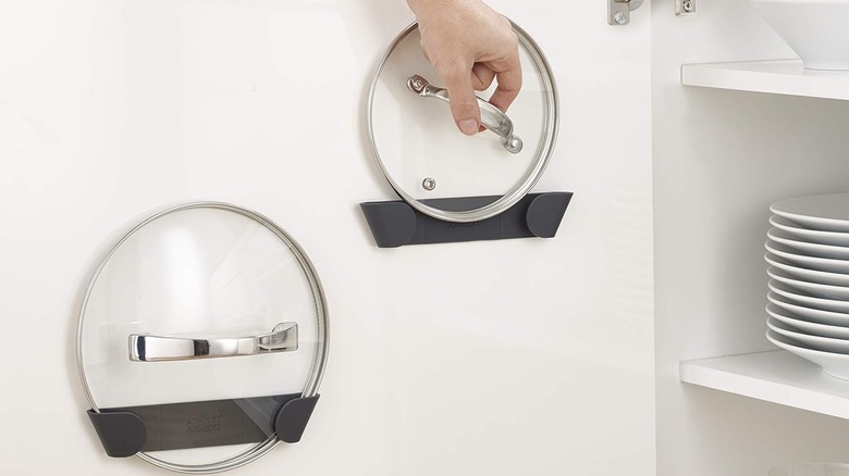 Two lids stored on adhesive lid holders on a cabinet door.